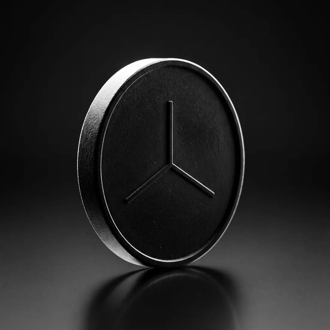 A black metal coin engraved with a three-armed emblem